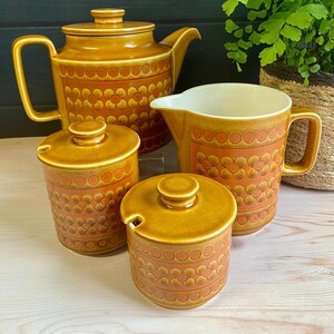 May include: A set of brown and orange ceramic teacups and teapot with a floral pattern. The set includes a teapot, a creamer, a sugar bowl, and two teacups.