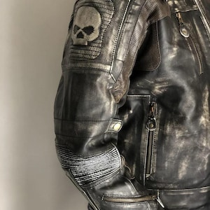 May include: Distressed black leather motorcycle jacket with a skull patch on the left shoulder and zippered pockets.