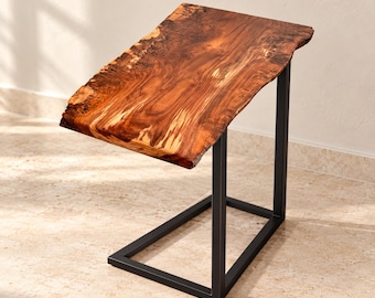 May include: A C-shaped side table featuring a natural live-edge wood slab top with prominent grain patterns and warm brown tones, supported by a sturdy, rectangular black metal frame base that provides stability and a clean, modern look.