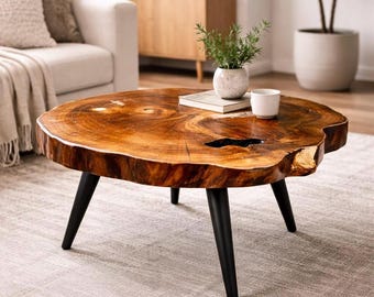 May include: A round coffee table featuring a natural wood slab top with a polished finish, visible wood grain, and a dark central void. The table is supported by three tapered black metal legs and sits on a light-colored textured area rug.