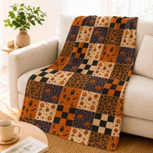 May include: A rectangular throw blanket featuring a patchwork design of alternating squares. The pattern includes orange pumpkins, black and orange checkered squares, leopard print, and small ghost, skull, and crescent moon motifs in orange and black.