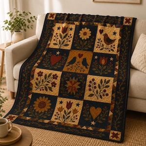 May include: A rectangular quilt featuring a grid of alternating dark navy blue and tan squares. The pattern includes appliqued motifs of sunflowers, tulips, birds, hearts, and stars in shades of red, gold, and green, finished with a decorative border.
