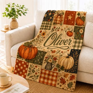 May include: A soft throw blanket featuring a patchwork design with orange pumpkins, autumn leaves, sunflowers, and plaid patterns. The centre displays the name Oliver in cursive script. The colour palette includes shades of orange, green, and cream.
