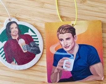 May include: Two car air fresheners featuring illustrations of men. The first air freshener is round and features a man with brown hair and a red shirt holding a coffee drink. The second air freshener is rectangular and features a man with brown hair and a blue shirt holding a white mug. Both air fresheners have a white background with a green and brown design.