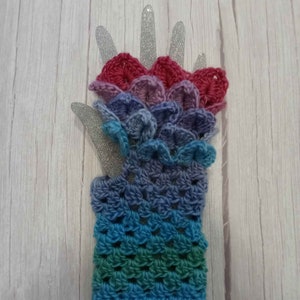 May include: A colorful crocheted fingerless glove with a scalloped design. The glove is made with a gradient of pink, purple, blue, and green yarn.