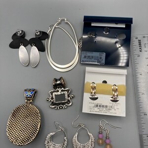May include: A collection of jewelry including silver-toned hoop earrings, black and silver drop earrings, two pendants, and two pairs of earrings on display cards. A ruler is visible on the right, showing a scale of approximately 5.5 inches in length.
