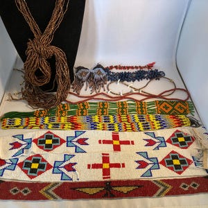 Könnte beinhalten: Eine Sammlung von Perlenschmuck, darunter Halsketten, Ohrringe und Gürtel. Die Halsketten sind braun und die Gürtel weisen farbenfrohe geometrische Muster in Rot, Blau, Gelb und Grün auf. Die Ohrringe sind blau und braun.