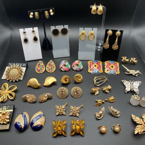 May include: A collection of assorted vintage-style earrings and brooches in gold-tone metal, featuring various shapes including floral, geometric, and butterfly designs, some accented with colorful enamel, faux pearls, and clear rhinestones.