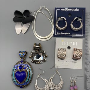 May include: A collection of jewelry including black and silver drop earrings, large silver hoop earrings, silver-plated hoop earrings on a card, two pendants, Trifari clip earrings with rhinestones, filigree hoop earrings, and beaded drop earrings.
