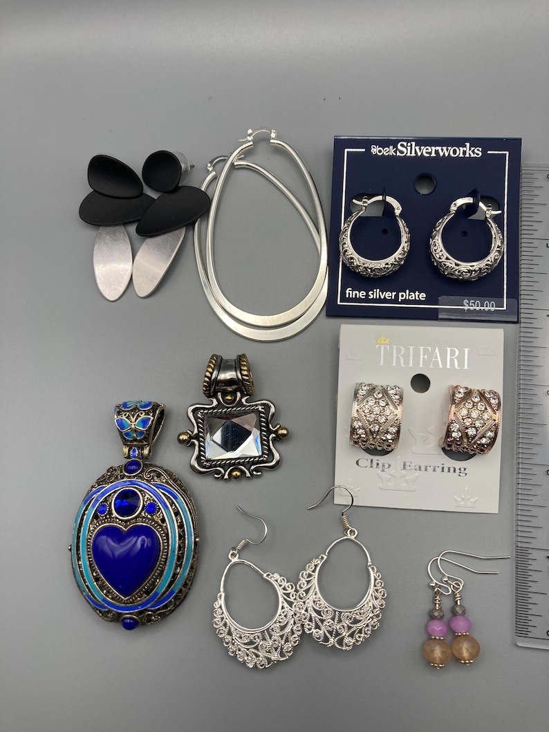 May include: A collection of jewelry including black and silver drop earrings, large silver hoop earrings, silver-plated hoop earrings on a card, two pendants, Trifari clip earrings with rhinestones, filigree hoop earrings, and beaded drop earrings.