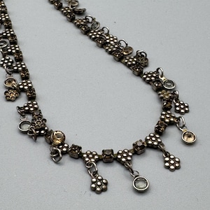 May include: A silver necklace with a delicate chain and multiple dangling charms. Each charm features a cluster of small, clear and amber-coloured rhinestones.