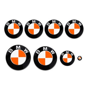 Puede incluir: Una colección de pegatinas con el logotipo de BMW en varios tamaños. Cada pegatina presenta un borde circular negro con el logotipo de BMW en el centro, un patrón de cuadros blanco y naranja y las letras "BMW".