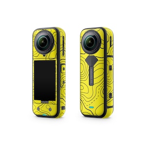 Puede incluir: Dos cámaras Insta360 X3 con un diseño de mapa topográfico amarillo. Las cámaras tienen una pantalla y lente negras, con el logotipo de Insta360. Las cámaras están sobre un fondo blanco.