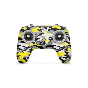 May include: A drone controller with a camouflage pattern in yellow, gray, and white. The controller has two joysticks, several buttons, and the DJI logo. The design is a modern take on a classic camouflage pattern.