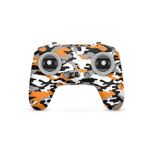 May include: A drone controller with a camouflage pattern in orange, gray, black, and white. The controller has two joysticks, several buttons, and the DJI logo. The design is a mix of digital and military camouflage.