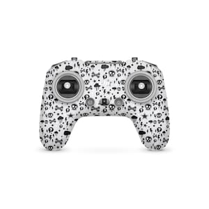 May include: A white drone controller featuring a black pattern of skulls, lightning bolts, question marks, and bones. The controller has two joysticks and several buttons, with the DJI logo.