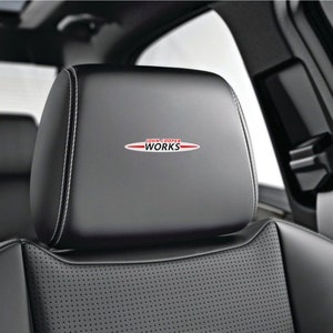 Peut inclure: Appuie-tête de siège de voiture en cuir noir avec un logo "JOHN COOPER WORKS" rouge et argent.