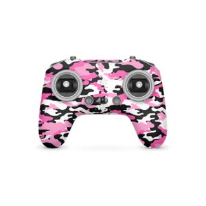 May include: A pink, black, and white camouflage-patterned drone controller. The controller has two joysticks, several buttons, and the DJI logo. The design is a vibrant mix of pink, black, and white, creating a bold and eye-catching aesthetic.