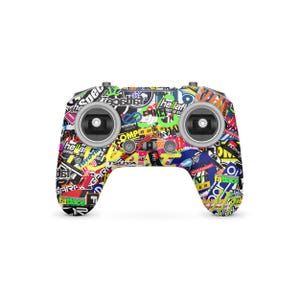 May include: A multi-colored remote control with a sticker-bomb design. The controller has two joysticks, several buttons, and a central power button. The stickers feature various fonts and colors, including red, yellow, green, and blue.