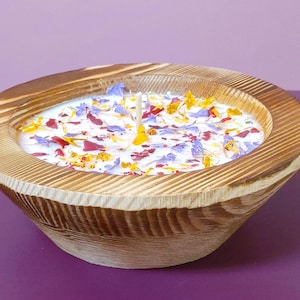 Puede incluir: Una vela en cuenco de madera con base de cera blanca, adornada con p&eacute;talos de flores de colores. El cuenco tiene un acabado de vetas de madera natural y una sola mecha. La vela es un art&iacute;culo decorativo.