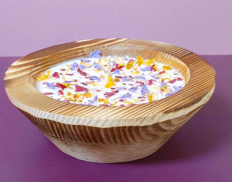 Puede incluir: Una vela en cuenco de madera con base de cera blanca, adornada con p&eacute;talos de flores de colores. El cuenco tiene un acabado de vetas de madera natural y una sola mecha. La vela es un art&iacute;culo decorativo.