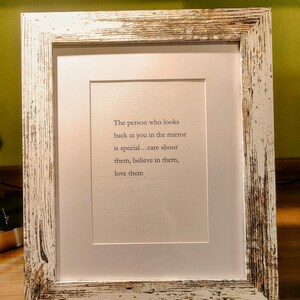Op de afbeelding: Een ingelijste print met een witte passe-partout en een verweerde wit en bruin houten lijst. De print bevat de tekst: "De persoon die in de spiegel naar je kijkt is speciaal... zorg voor ze, geloof in ze, houd van ze."