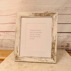 Op de afbeelding: Een ingelijste print met een wit, verweerd houten frame. De print heeft een witte passe-partout en een lichtroze achtergrond met de tekst: "De persoon die in de spiegel naar je kijkt is speciaal... zorg voor hen, geloof in hen, houd van hen."