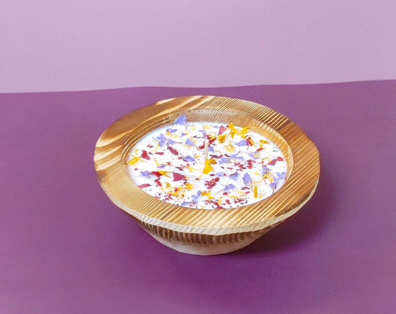 Puede incluir: Un cuenco de madera lleno de una sustancia blanca y p&eacute;talos de flores de colores. El cuenco tiene un acabado de vetas de madera natural y est&aacute; sobre una superficie p&uacute;rpura. Los p&eacute;talos son rojos, amarillos y azules.