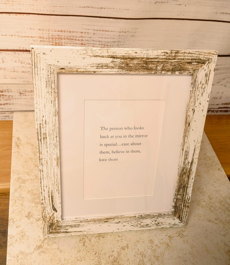 Op de afbeelding: Een witte, verweerde houten fotolijst met een citaat in zwarte tekst. Het citaat luidt: "De persoon die je in de spiegel aankijkt is speciaal... zorg voor hen, geloof in hen, houd van hen."