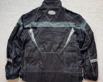 May include: Black and grey jacket with a silver logo on the back. The jacket has multiple pockets and a zip closure.