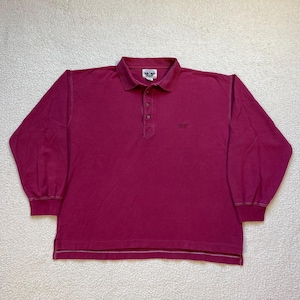 Puede incluir: Un polo burdeos de manga larga con cuello y tapeta de tres botones. La camisa presenta un pequeño logotipo en el pecho y un dobladillo a rayas. Las mangas tienen puños acanalados.