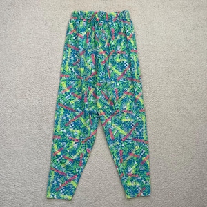 May include: Bright green, blue, and pink patterned pants. The pants have an elastic waistband and a colorful geometric design. The fabric appears to be lightweight, suitable for casual wear. The pants are laid flat on a neutral surface.