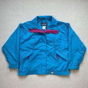 Könnte beinhalten: Eine blaue und rosafarbene leichte Jacke mit Reißverschluss und einem kleinen Logo-Patch mit der Aufschrift "West Ridge" auf der linken Brust.