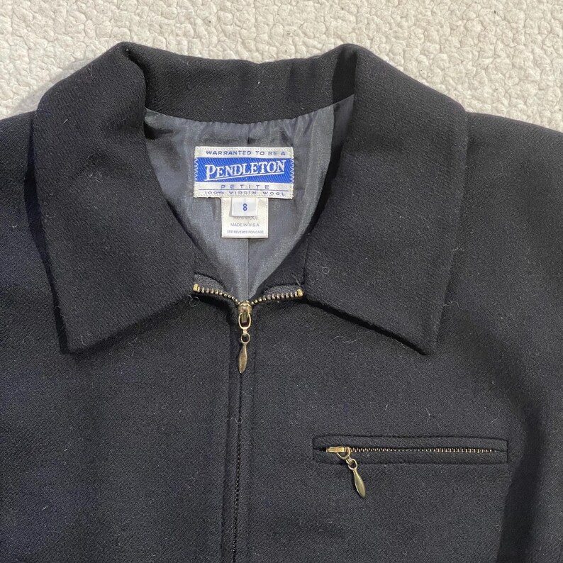 May include: Black wool jacket with a collar, a zipper closure, and a small zippered pocket. The jacket features a label that reads "Pendleton Petite". The jacket is size 8.