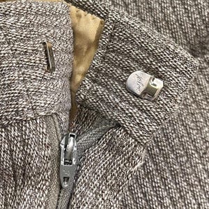 Peut inclure: Gros plan sur un pantalon en tweed marron et blanc. L'image montre la fermeture éclair, un fermoir métallique et un bouton avec le mot "Talon" dessus. Le pantalon est fait d'un tissu texturé.