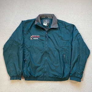 May include: A dark green jacket with a zipper closure and a fleece-lined collar. The jacket has a logo on the left chest that reads "Skamania Pete's Duck Inn Skamania Washington".