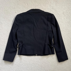 May include: A black blazer with a notched lapel and long sleeves. The back of the jacket features a tailored design with decorative buttons and a fitted silhouette. The blazer is made of a smooth, dark fabric.