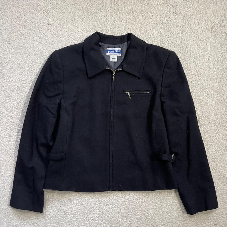 May include: A black jacket with a zipper closure, a small zippered pocket on the chest, and a collar. The jacket has a tailored fit and a small buckle detail on the sleeves. The brand name "Pendleton" is visible on the label.
