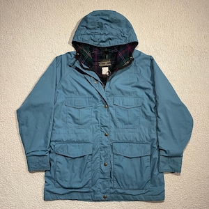 May include: A teal-colored hooded jacket with a button-up front and multiple pockets. The jacket features a plaid lining visible at the hood's interior. The jacket has a classic design, suitable for outdoor wear. The jacket is made of a durable, weather-resistant material.