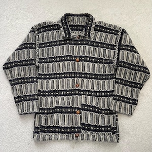 May include: A patterned button-down jacket in black, white, and grey. The jacket features a collared neckline, long sleeves, and wooden buttons. The fabric is a woven material, suitable for cooler weather. The jacket's length is approximately 60 cm.