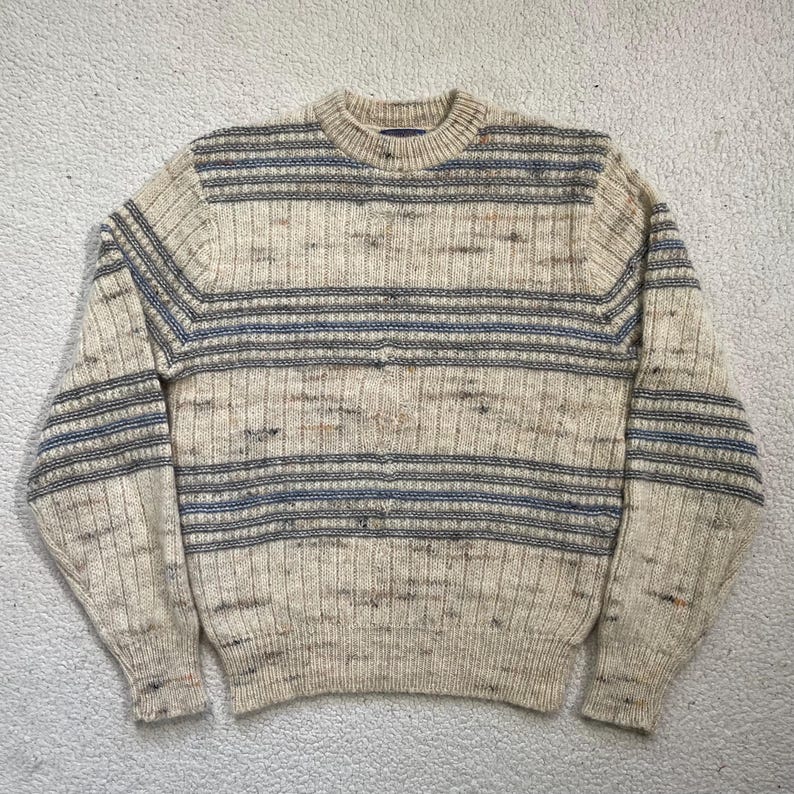 Pode incluir: Camisola creme com riscas horizontais azuis e cinzentas. A camisola tem uma textura canelada e gola redonda. As mangas e o corpo t&ecirc;m uma cor consistente com as riscas. Uma pe&ccedil;a de roupa quente e confort&aacute;vel para climas mais frios.