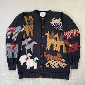 May include: Black cardigan sweater with various animal appliqués, including elephants, giraffes, dogs, and sheep. The sweater has a button-up front with red buttons and ribbed cuffs and hem. The animals are in various colors and patterns.