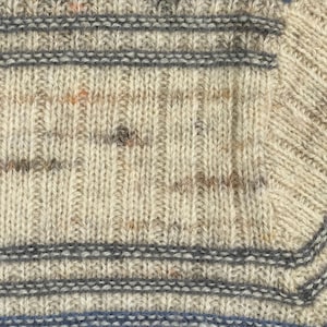 Pode incluir: Close-up de um tecido de malha com apar&ecirc;ncia texturizada. O fio &eacute; uma mistura de bege, cinza e manchas de outras cores. Listras cinzas horizontais e uma listra azul adicionam detalhes ao design. A malha tem uma textura canelada.