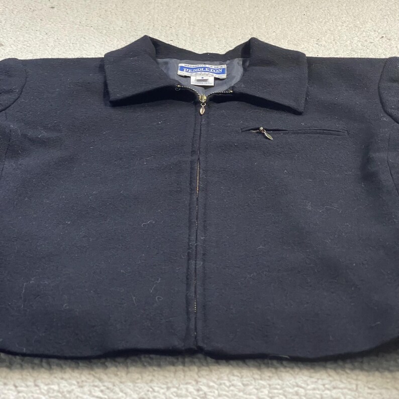 May include: A black wool jacket with a collar and a full-length zipper. The jacket has a small pocket on the chest and a label that reads "Pendleton". The jacket is a size M.