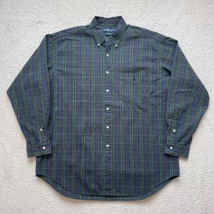 May include: A long-sleeved plaid button-down shirt with a small embroidered logo on the left chest pocket. The shirt is in a blue, green, and red plaid pattern.