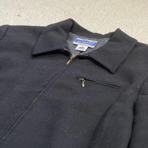 May include: A black wool jacket with a collar and a full-length zipper. The jacket has a small pocket on the chest and a label that reads "Pendleton". The jacket is a classic style.