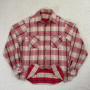 May include: A red, white, and beige plaid flannel shirt with two front pockets and button closures. The shirt has a classic collar and buttoned cuffs. The bottom hem is visible, showing a red and beige striped lining.