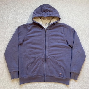 Puede incluir: Una sudadera con capucha de color morado con forro polar, cremallera, bolsillo canguro y un pequeño logotipo en la parte inferior derecha.