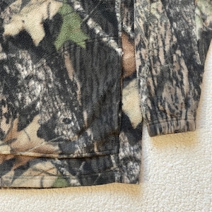 May include: A brown, green, and beige fleece jacket with a camouflage pattern. The jacket has a zipper closure and a stand-up collar.