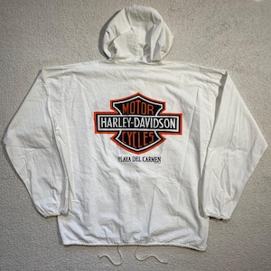 May include: White Harley-Davidson windbreaker jacket with a hood and drawstring. The back features the Harley-Davidson Cycles logo in black, orange, and white, with "Playa Del Carmen" printed below. The jacket has long sleeves and elastic cuffs.